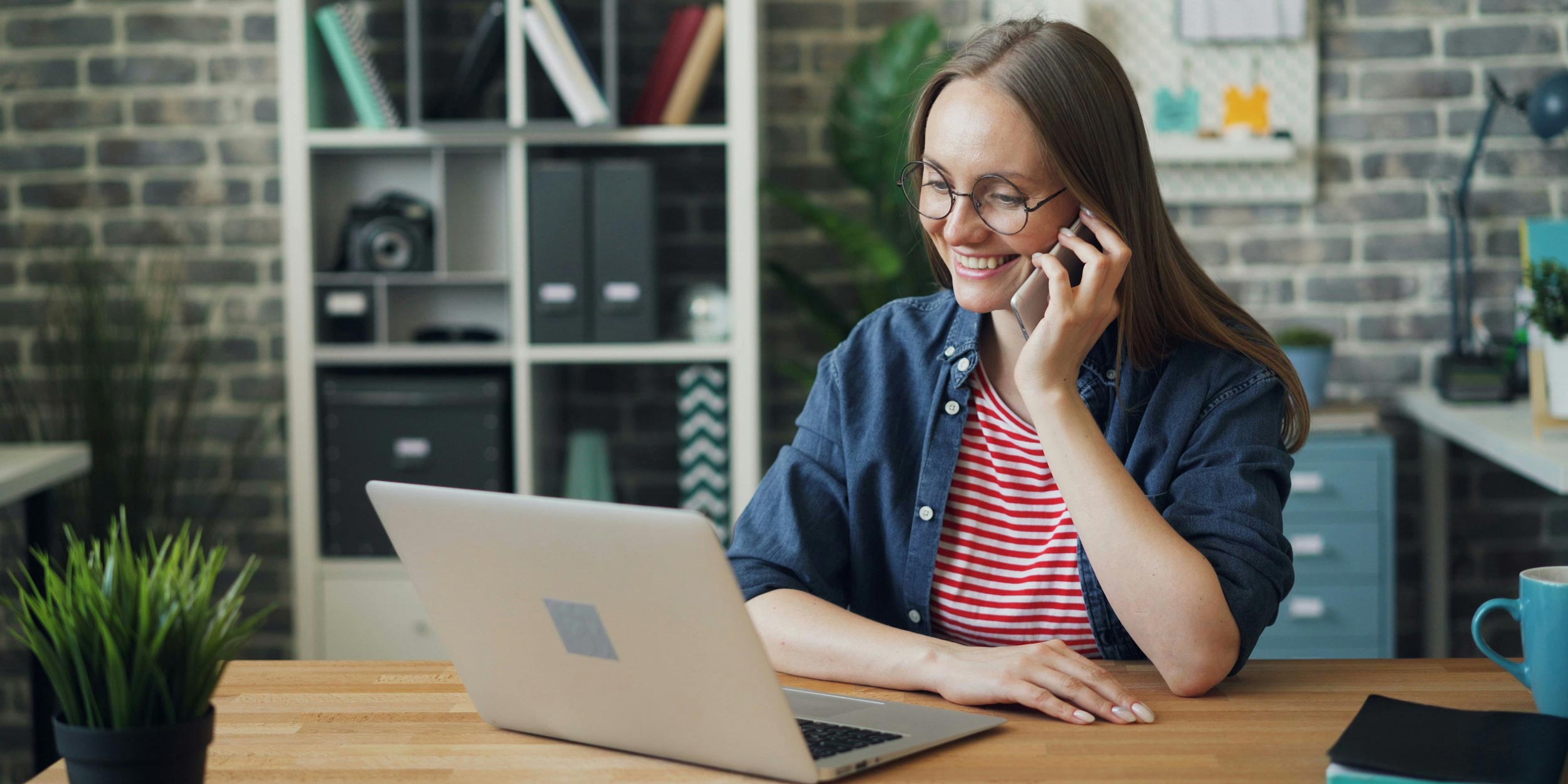 Woman on phone call smiling while working on laptop at desk