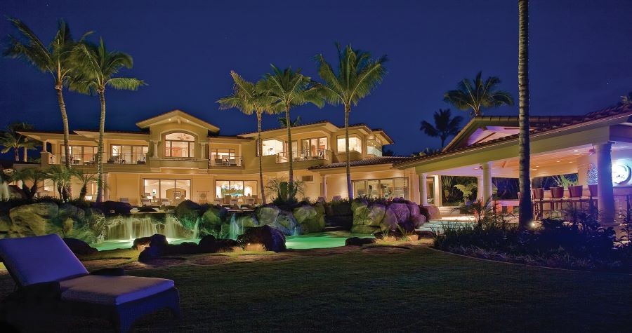 Front of home at night with expansive yard and water features highlighted with outdoor lights.