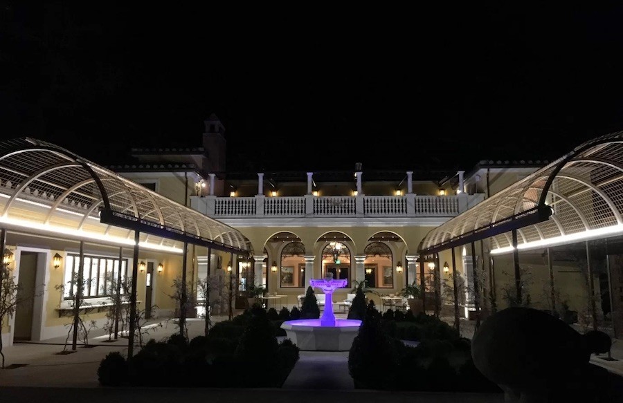 outdoor view of a winery in the evening. A fountain is lit with purple lights, and walkways are illuminated.