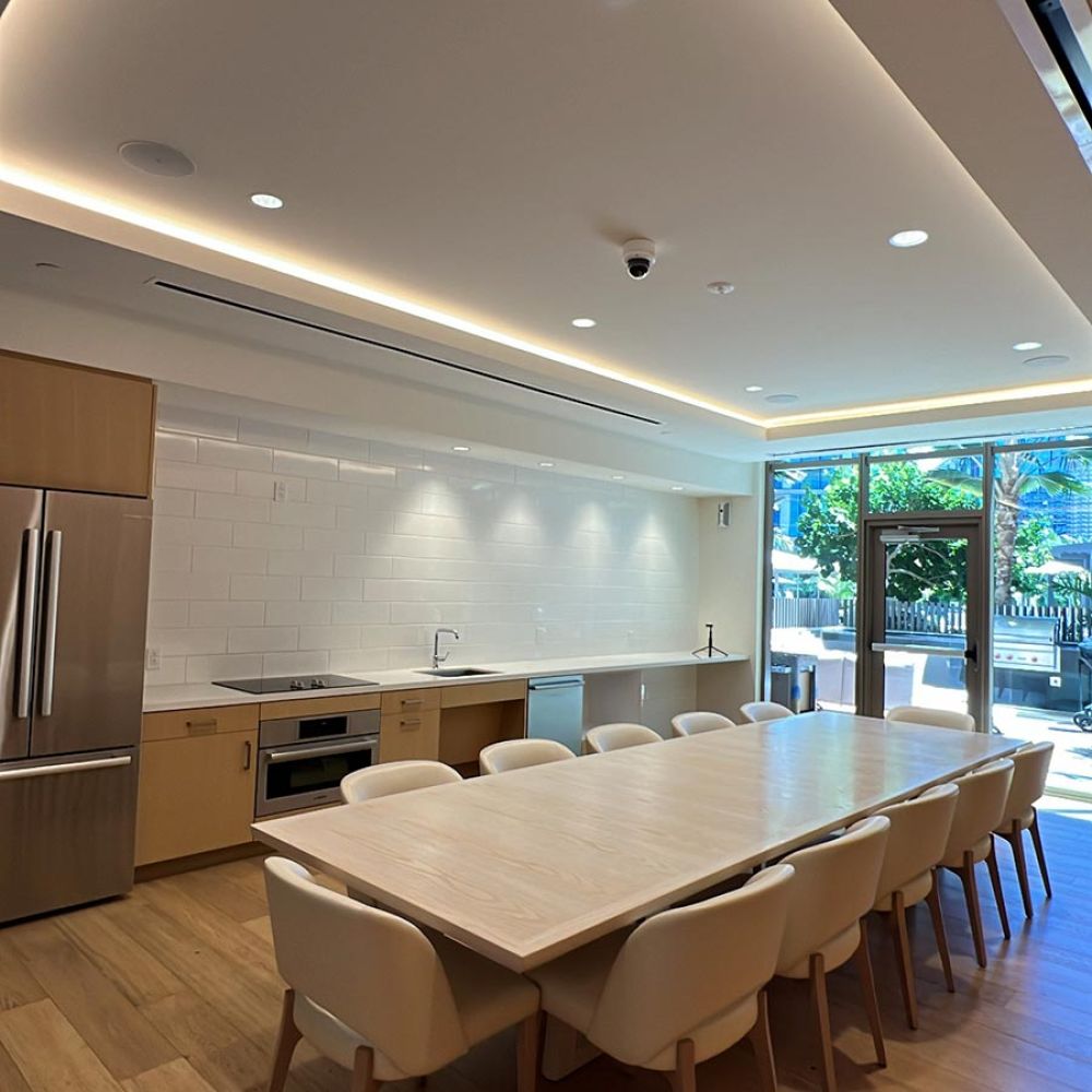Modern kitchen with long dining table, light wood finishes, and large glass doors