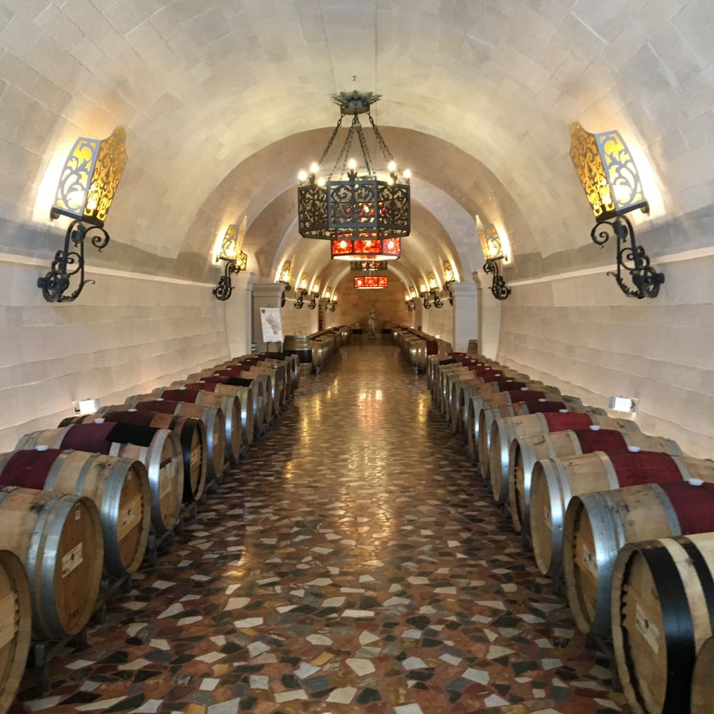 Wine barrels lined in an arched stone cellar with decorative lights and tiled floor